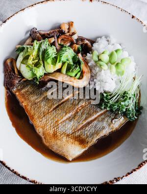 Gegrillter Fisch mit flauschigem Reis und Gemüse der Saison, kunstvoll auf einem Teller angeordnet Stockfoto