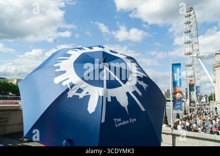 Großbritannien Wetter, 14. August 2025: Da die Temperaturen im Zentrum Londons wieder 27 Grad erreichten, verwenden Ticketverkäufer für Sightseeing-Busse einen London Eye Schirm als Sonnenschirm mit dem eigentlichen London Eye direkt dahinter und einem Werbebanner für das Paddington Bear Experience. Quelle: Anna Watson/Alamy Live News Stockfoto