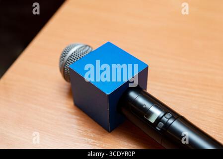Nahaufnahme eines Mikrofons mit markanter blauer quadratischer Windschutzscheibe auf einem Holztisch. Ideal für Medien, Rundfunk- oder Interviewthemen Stockfoto