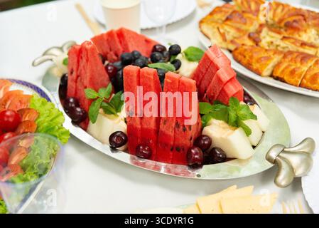 Eine lebhafte Sommerobst-Platte mit frisch geschnittenen Wassermelonen, Trauben und Honigtau, garniert mit Minze. Perfekt für Versammlungen und festliche Okka Stockfoto