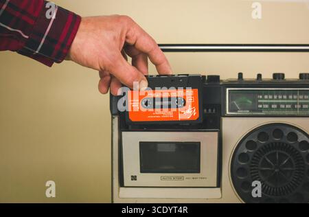 Madrid, Spanien 1. Juni 2023 Einlegen eines orangen Kassettenbandes in eine Vintage-Boombox. Eine Hand, die ein Kassettenband in eine Vintage-Boombox einsteckt und festnimmt Stockfoto