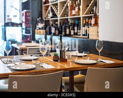 Elegantes Ambiente in einem spanischen Restaurant mit Weingläsern, Tellern, Besteck und Weinflaschen auf Regalen im Hintergrund Stockfoto