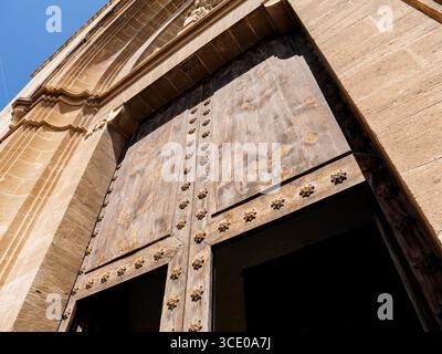 Flacher Blick auf eine große historische Holztür mit dekorativen Metallknöpfen in einer Steinfassade unter klarem blauen Himmel in Pollenca, Spanien Stockfoto