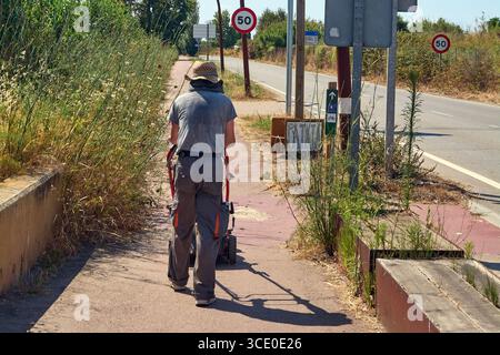 Viladecans. Barcelona - 14. August 2025: Ein Mann von hinten schiebt an einem sonnigen Tag einen Handwagen in die Nähe der Straße. Das Bild ist ideal für die Darstellung von Konz Stockfoto