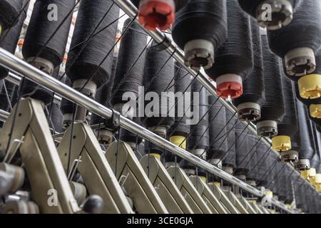 Reihen schwarzer Garnkonen auf einer automatischen Spinnlinie in einer Textilfabrik, die moderne Produktions- und Präzisionsausrüstung zeigt. Stockfoto