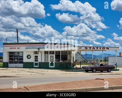 The Station mit Service Bay: Alte historische Retro-Tankstelle, Tankstelle, Tankstelle; amerikanisches Auto parkt davor; sonniger Himmel mit Wolken Stockfoto