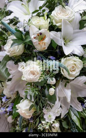 Ein wunderschönes Blumenarrangement mit weißen Lilien und weißen Rosen, ergänzt durch verschiedene grüne Blätter und dezente Akzentblumen, angeordnet in A Stockfoto