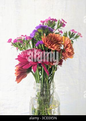 Ein lebhaftes Sommerbouquet mit rosa und orangefarbenen Chrysanthemen, violetter Statice und grünen Stielen, arrangiert in einem Gläser Stockfoto