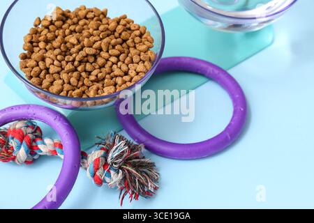 Schüssel mit Trockenfutter und Kauspielzeug auf blauem Hintergrund Stockfoto