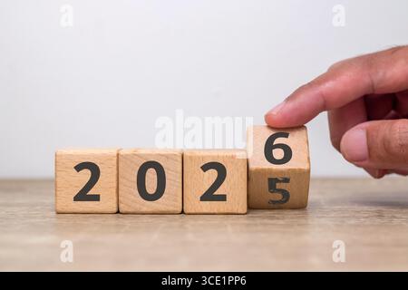 Handumschlag von 2025 bis 2026 auf Holzblöcken, wobei die Zahl fünf bereits verblasst ist. Wende des neuen Jahres. Neujahrsvorsatz. Stockfoto