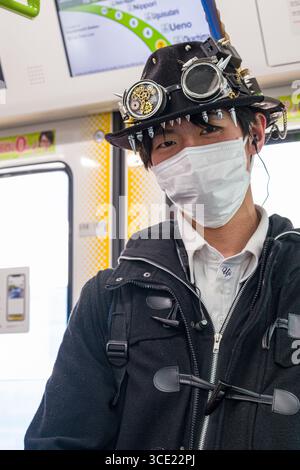 Junge japanische Mann mit einem Mundschutz und eine Steam-punk hat mit Spikes und Schutzbrille in einem pendlerzug stehend, Tokio, Honshu, Japan Stockfoto