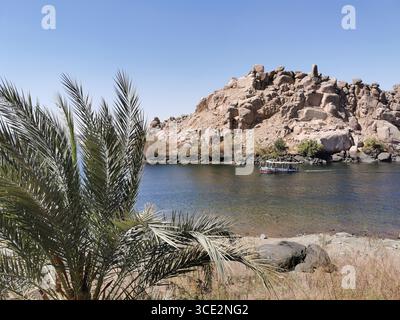 Das Touristenboot passiert große Granitinseln in der Nähe des Philae Tempels in Assuan, die teilweise vom aufsteigenden Nilwasser des British Dam untergetaucht sind. Stockfoto