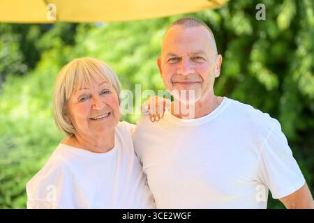 Glückliches älteres Paar posiert zusammen in einem sonnigen Garten. Stockfoto