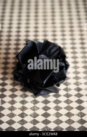 Zerknittertes schwarzes Papier auf Vintage-Schachbrettoberfläche, abstraktes Draufsicht-Konzept Stockfoto