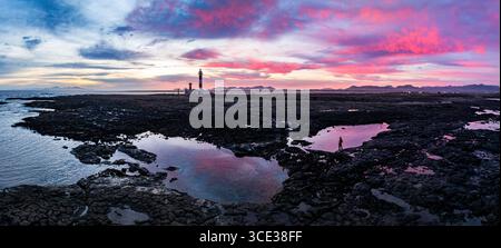 Wanderer, der den romantischen Himmel bei Sonnenaufgang über dem Leuchtturm El Toston betrachtet, aus der Luft, Fuerteventura, die Kanarischen Inseln, Spanien Stockfoto