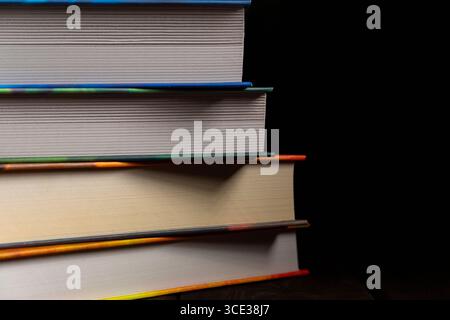 Seitenansicht eines Stapels dicker Hardcover-Bücher mit bunten Kanten, ordentlich vor schwarzem Hintergrund angeordnet. Ideal für Bildungskonzepte, Lear Stockfoto
