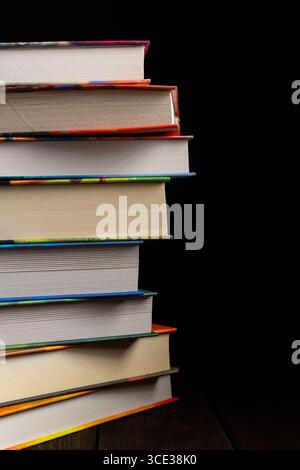 Ein vertikaler Stapel dicker Hardcover-Bücher mit bunten Bindungen, platziert auf schwarzem Hintergrund. Ideal für Themen wie Bildung, Lesen, Bibliotheken Stockfoto