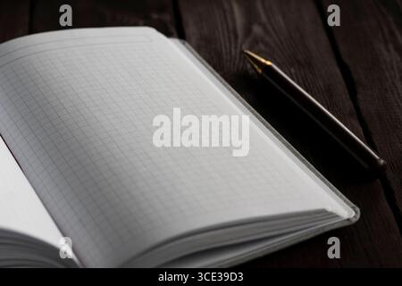 Saubere und minimale Nahaufnahme eines offenen Notizbuchs mit Rasterseite und rotem Lesezeichen auf einer dunklen Holzoberfläche. Ein verschwommener Stift liegt subtil in der Th Stockfoto