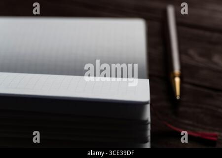 Ein offenes Notizbuch mit gerasterten Seiten liegt auf einem rustikalen dunklen Holztisch neben einem Stift mit goldener Spitze und erinnert an einen gemütlichen Arbeitsplatz, der zum Schreiben oder Skizzieren bereit ist Stockfoto