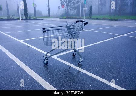 Ein verlassener Einkaufswagen auf einem nebeligen Parkplatz, ein Gefühl der Einsamkeit. Stockfoto