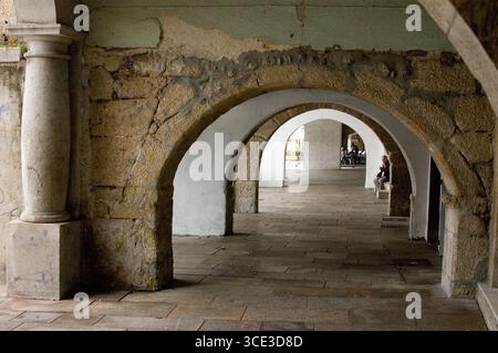 Ein Mann sitzt auf einer Bank unter einem Bogengang. Stockfoto