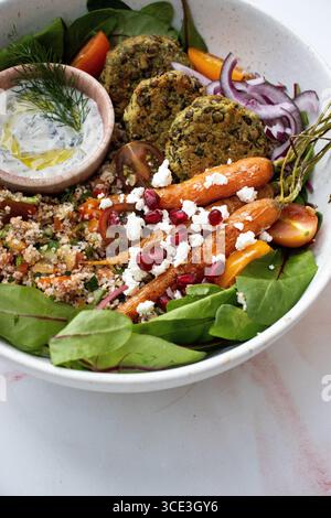 Gesunde, mediterrane Salatschüssel mit frischem Spinat, gebratenen BabyKarotten, garniert mit zerbröckeltem Feta und Granatapfelkernen, Quinoa Stockfoto