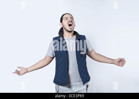 Wütender Mann, der mit offenen Armen auf isoliert schreit. Gestresster Mann, der schreiend mit ausgestreckten Armen auf weißem Hintergrund schreiend Stockfoto
