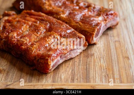 Rohe, gewürzte und marinierende Schweinerippchen oder Spare Rippchen auf einem hölzernen Küchenbrett. Nahaufnahme, keine Leute Stockfoto