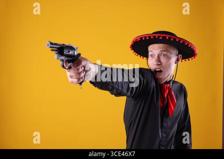 Emotionaler Mann in schwarzem Flamenco-Hut mit Pistole auf gelbem Hintergrund Stockfoto