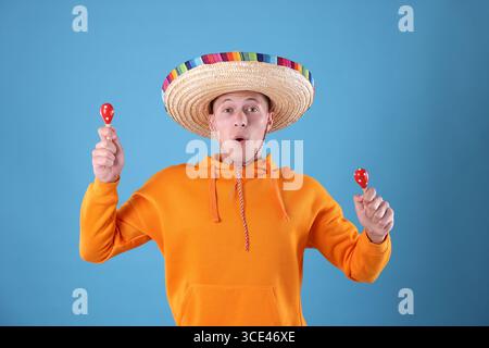 Emotionaler Mann mit Sombrero-Hut, der Maracas auf hellblauem Hintergrund spielt Stockfoto