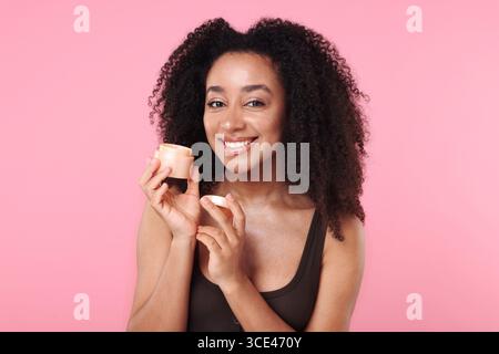 Schöne brasilianische Frau mit einem Glas Kollagencreme auf rosa Hintergrund Stockfoto