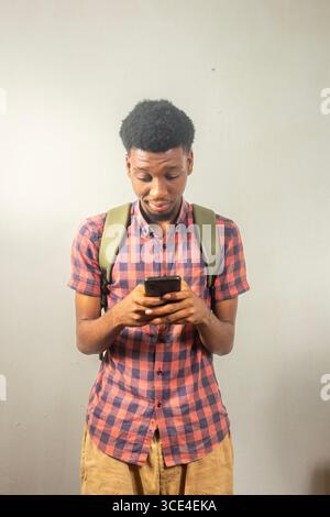 Schwarzer Teenager, der einen Rucksack mit Smartphone trägt, der zurück in die Schule, Technik, Kommunikation, Online-Verbindung, E-Learning, Dating, Akademiker Stockfoto