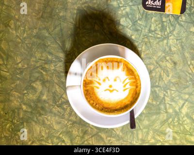 Blick von oben auf eine Kaffeetasse mit Latte Art, die ein Katzengesicht auf einem strukturierten grünen Tisch darstellt malaysia Stockfoto