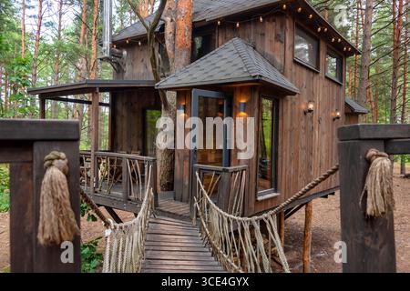 Einzigartig gestaltetes Holzbaumhaus mit einladendem Brückeneingang, umgeben von üppigem Wald. Perfekt für Naturrezepte, Öko-Frien Stockfoto