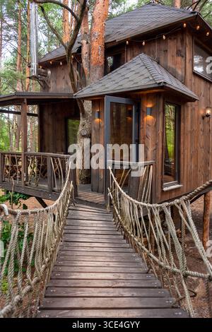 Einzigartig gestaltetes Holzbaumhaus mit einladendem Brückeneingang, umgeben von üppigem Wald. Perfekt für Naturrezepte, Öko-Frien Stockfoto