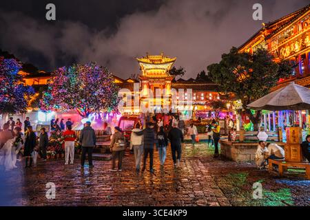 Lijiang, China - 24. Oktober 2024: In der Altstadt von Lijiang, einem historischen Viertel, versammeln sich Menschenmassen in der Nähe eines traditionellen Tors und Marktplatzes unter bunten Lichtern Stockfoto
