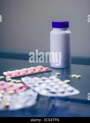 Eine Sammlung von bunten Blisterpackungen liegt verstreut auf einer reflektierenden Oberfläche, begleitet von einer weißen Flasche mit violettem Verschluss. Verschiedene Pillen sind Visi Stockfoto