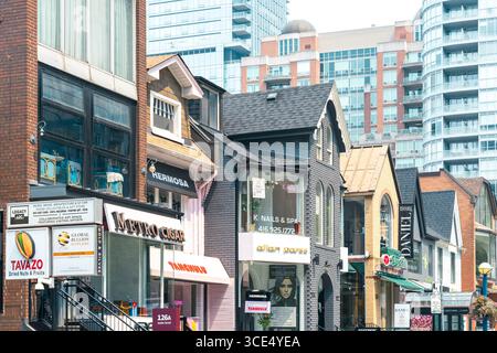 Geschäfte und kleine Unternehmen mit farbenfrohen Fassaden säumen einen geschäftigen Geschäftsabschnitt in Yorkville, der sich vor hohen Wohnhäusern befindet. Stockfoto