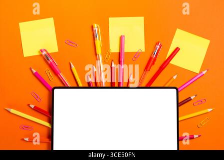 Digitales Tablet, Haftnotizen und farbenfrohe Schulutensilien auf leuchtend orangefarbenem Hintergrund. Perfekt für Planungs- und Bildungskonzepte. Stockfoto