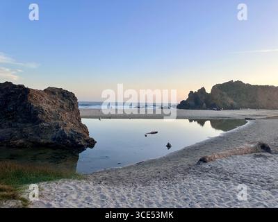 Eine ruhige Szene am Pfeiffer Beach in Big Sur, Kalifornien, mit einer friedlichen Lagune, die die felsigen Klippen und den pastellfarbenen Abendhimmel reflektiert. Stockfoto