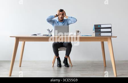 Schockiert arabischen Kerl greifen Kopf mit Laptop Stockfoto