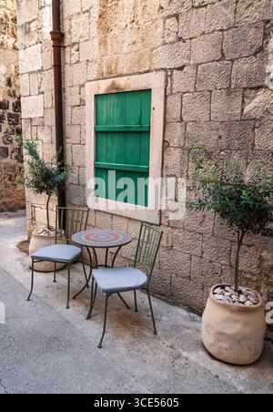 Eine gemütliche Ecke für zwei Personen in einer historischen mediterranen Gasse mit Mosaiktisch, Stühlen und Olivenbäumen. Malerisches Café im Freien mit Stockfoto