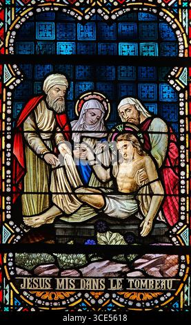 Rochefort, Belgien - 23. Juli 2025: Buntglasfenster, in dem Jesus nach der Kreuzigung in das Grab gelegt wird, mit Maria und anderen Jüngern Stockfoto