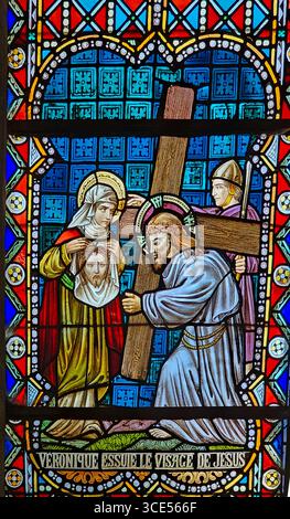 Rochefort, Belgien - 23. Juli 2025: Buntglasfenster, das die Heilige Veronika zeigt, die Jesus ihren Schleier anbietet, um sein Gesicht abzuwischen, und sein Bild enthüllt. Stockfoto