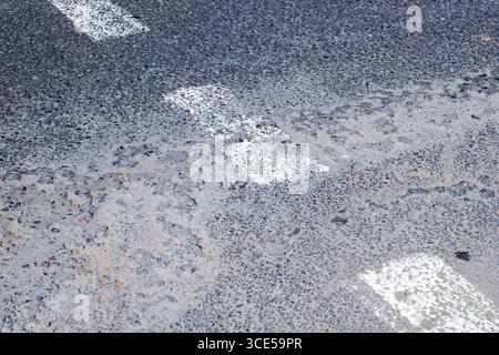 Nahaufnahme einer strukturierten Straßenoberfläche mit verblassten weißen Linienmarkierungen, die ein abstraktes Muster erzeugen. Perfekt für städtische und künstlerische Projekte. Stockfoto