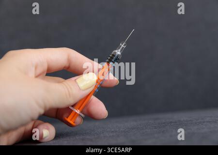 Diese Abbildung zeigt eine Nahaufnahme einer Hand, die mit einem orangefarbenen Kolben eine Spritze fasst, wobei die Nadel und die Messschritte auf dem Transpar sichtbar werden Stockfoto