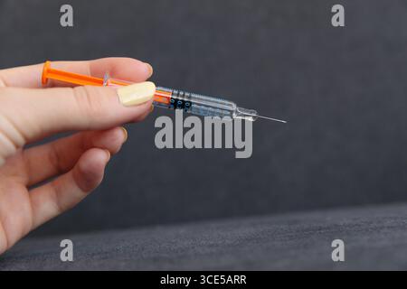 Dieses Bild zeigt eine Hand, die eine Spritze mit einer leuchtend orangefarbenen Kappe greift und das wichtige medizinische Instrument zeigt, das für Injektionen, Impfstoffe und verwendet wird Stockfoto