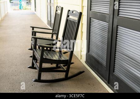 Zwei schwarze Holzschaukelstühle ruhen auf einer sonnendurchfluteten Veranda und schaffen eine friedliche und einladende Südstaatenlandschaft. Stockfoto