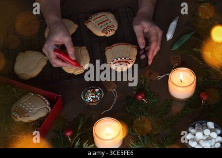 Frauenhände dekorieren hässliche Weihnachtspullover-Kekse mit Glasur Stockfoto