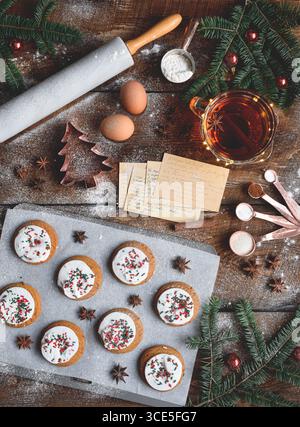 Blick von oben nach unten auf Weihnachtskekse auf Backblech umgeben von Dekorationen, Pin, Rezeptkarten, auf rustikalem hölzernem Hintergrund Stockfoto